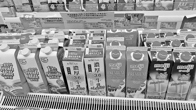 Cartons of various milk brands and types neatly arranged on a refrigerated supermarket shelf.