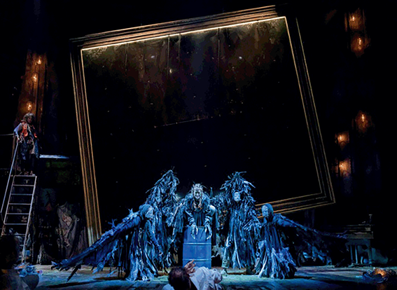 A woman portraying Ariel stretches out long wings made of black rubbish bin bags, supported by four other actors.