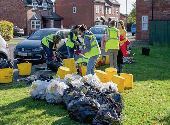 Volunteers wearing neon yellow (high visual) vests collect bags of rubbish outside in Stratford on Avon.
