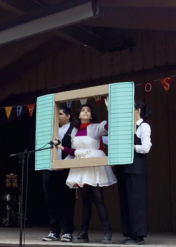 A woman portraying Juliet looks out from a cardboard window while standing on an outdoor stage.