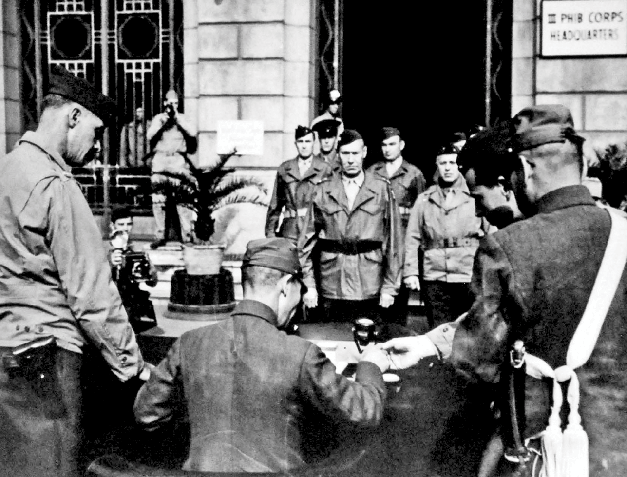 Major General Keller Rockey, standing in the center of the picture in front of the Three, Amphibious Corps Headquarters, is accompanied by his Chief-of-Staff, General William Worton. See long description.