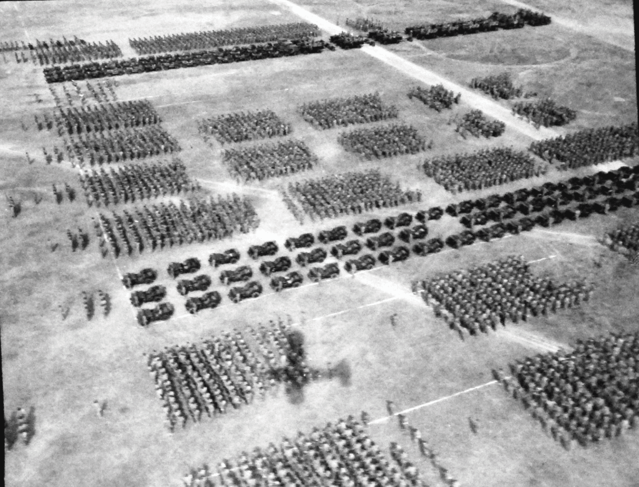 A ceremonial formation of U.S. infantry and vehicles is photographed by an aircraft in the air over a spacious racecourse.