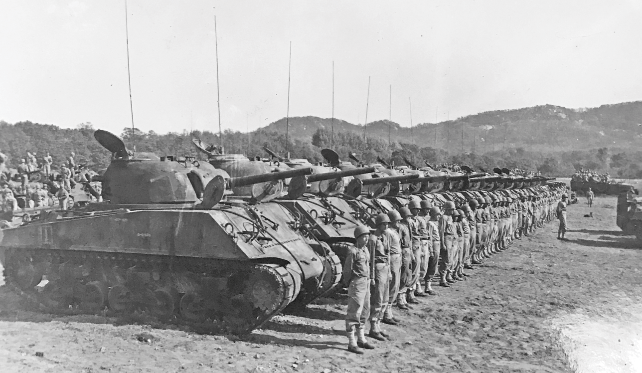 A row of M 4 Sherman tanks stands with their crew, who are lined up in front of them.