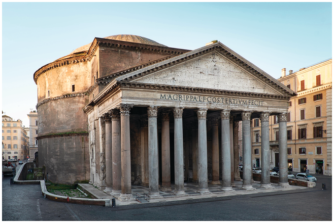 The façade of the Pantheon in a three-quarters view shows a row of 8 marble columns across the front and the curved brick wall on the left. The columns support an architrave with a inscription and a triangular pediment above it.