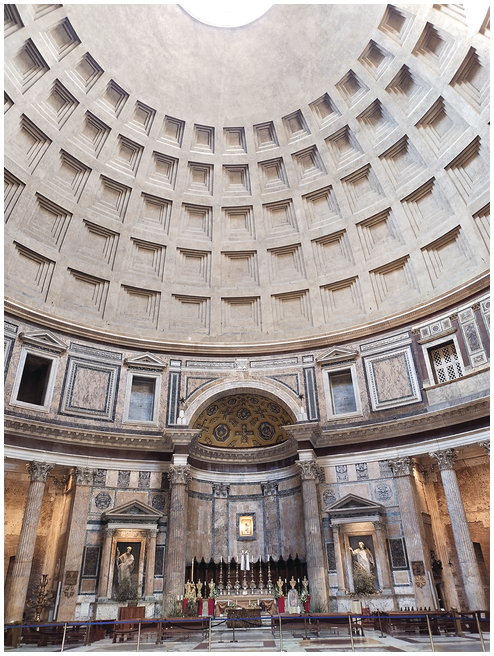 An interior view of the domed pantheon. The upper portion shows dome coffers and a portion of the open oculus. At ground level are the church pews and the altar, with marble columns, niches with statues, and a colorful marble inlay on the walls.