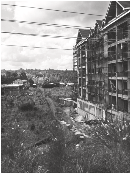 A photo of a high-rise apartment block under construction surrounded by fields and low-rise buildings in the distance. See long description.