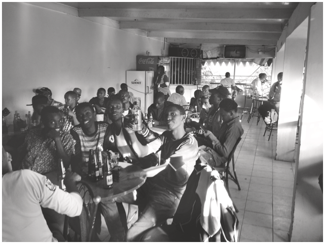 A photo of young men seated in a bar watching football. See long description.