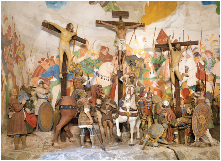 A multi-figure polychrome sculptural group in front of a frescoed wall. See long description.