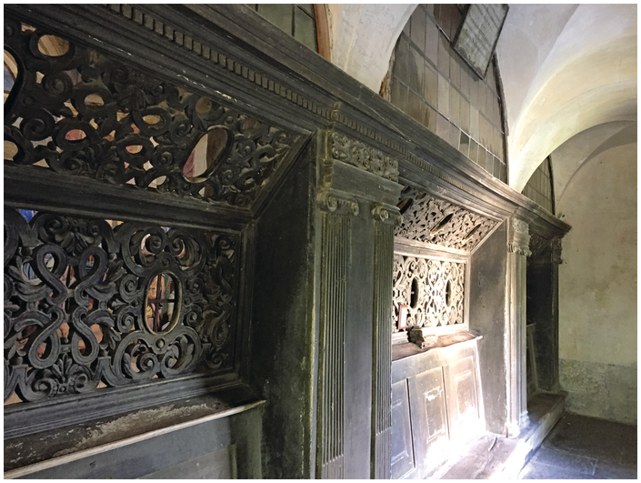 A wall inset with ornately carved wooden screens. Each contains several oval holes through which a viewer could look to see the sculptural scenes that lay behind, not visible here.