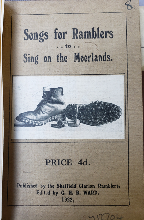 The cover of a pocket-sized songbook with an illustration of a pair of walking boots and a pair of pipes (for smoking) in the center against a light background. See long description.
