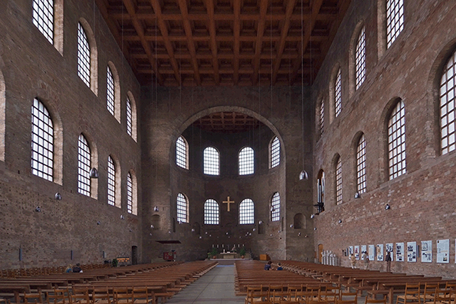 A view of the interior of the Constantinian Basilica in Trier. It is a large space ending in an apse. The lateral walls are pierced with big windows, and it has a coffered roof.