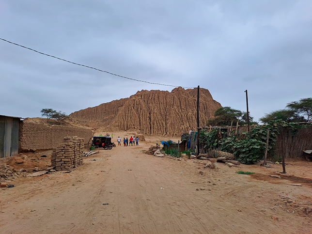 A view of Huaca “El Pueblo” pyramid mound located centrally in the village of Túcume, surrounded by modern buildings and vegetation.