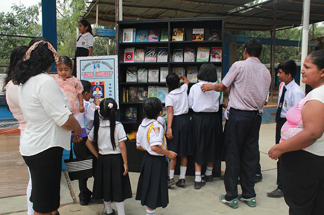 Children, accompanied by adults, picking up books from the bookshelves filled with donated educational materials at the Liceo Aguirre La Pintada school.
