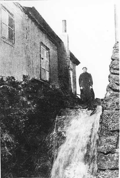 A woman standing by a house and a small waterfall.