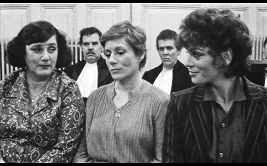 Three women, seated shoulder to shoulder in business attire, shown from the waist up. See long description.