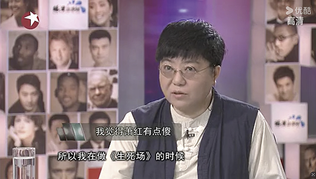Tian Qinxin appears in an interview with Yang Lan. She wears short hair, glasses, and a dark vest over a light shirt, presenting a composed and masculine look while discussing her work on The Field of Life and Death.