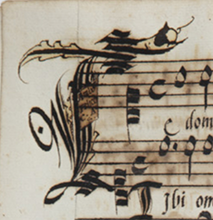 A small section of a 16th-century music manuscript, with a large letter T at the beginning of two staff systems of music. The T has a small plaque on its upright, on which is inscribed the words, ‘Ambo felice, C.A.S’. See long description.