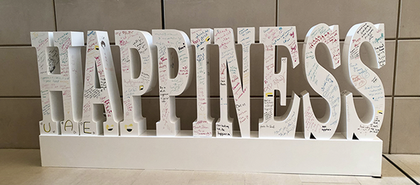A large sculpture in the university promenade. The sculpture spells the word happiness in English. It has handwritten translingual messages and pictures covering it.