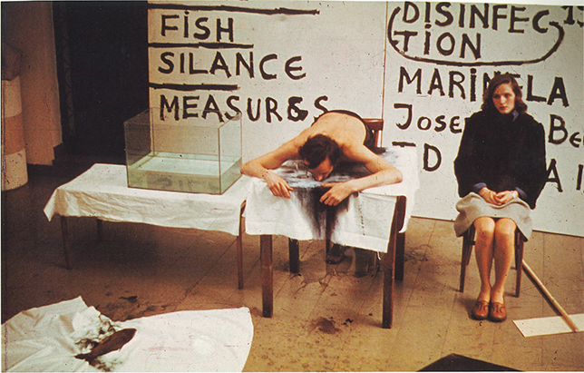 Raša Todosijević with his partner Marinela Koželj perform Drinking Water, Inversions, Imitations, and Contrasts at the Fourth April Encounters on 19 April 1975 at the Student Cultural Center. See long description.
