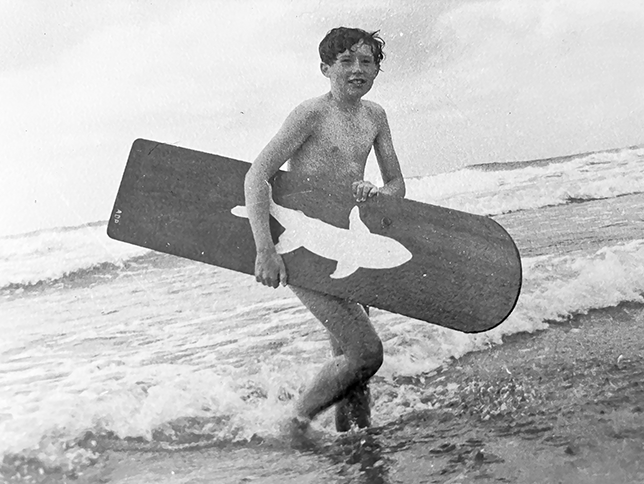 The author as a young boy walking out of the sea carrying a surfboard.