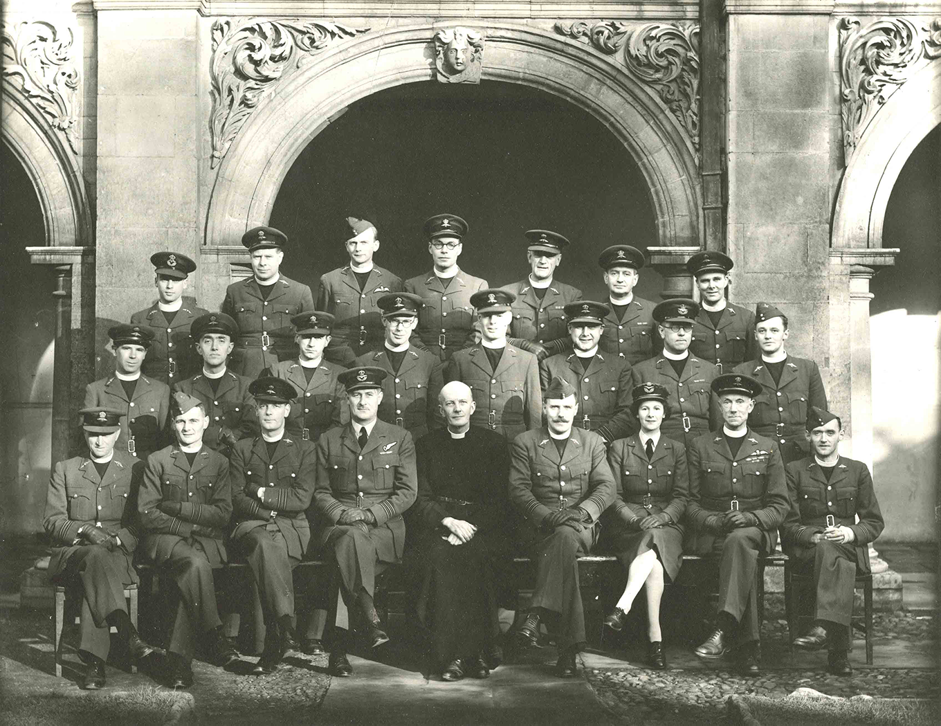 Photo showing a group of uniformed R A F chaplains and officers seated and standing in four rows in front of arched stonework at Magdalene College, Cambridge, November 1943.
