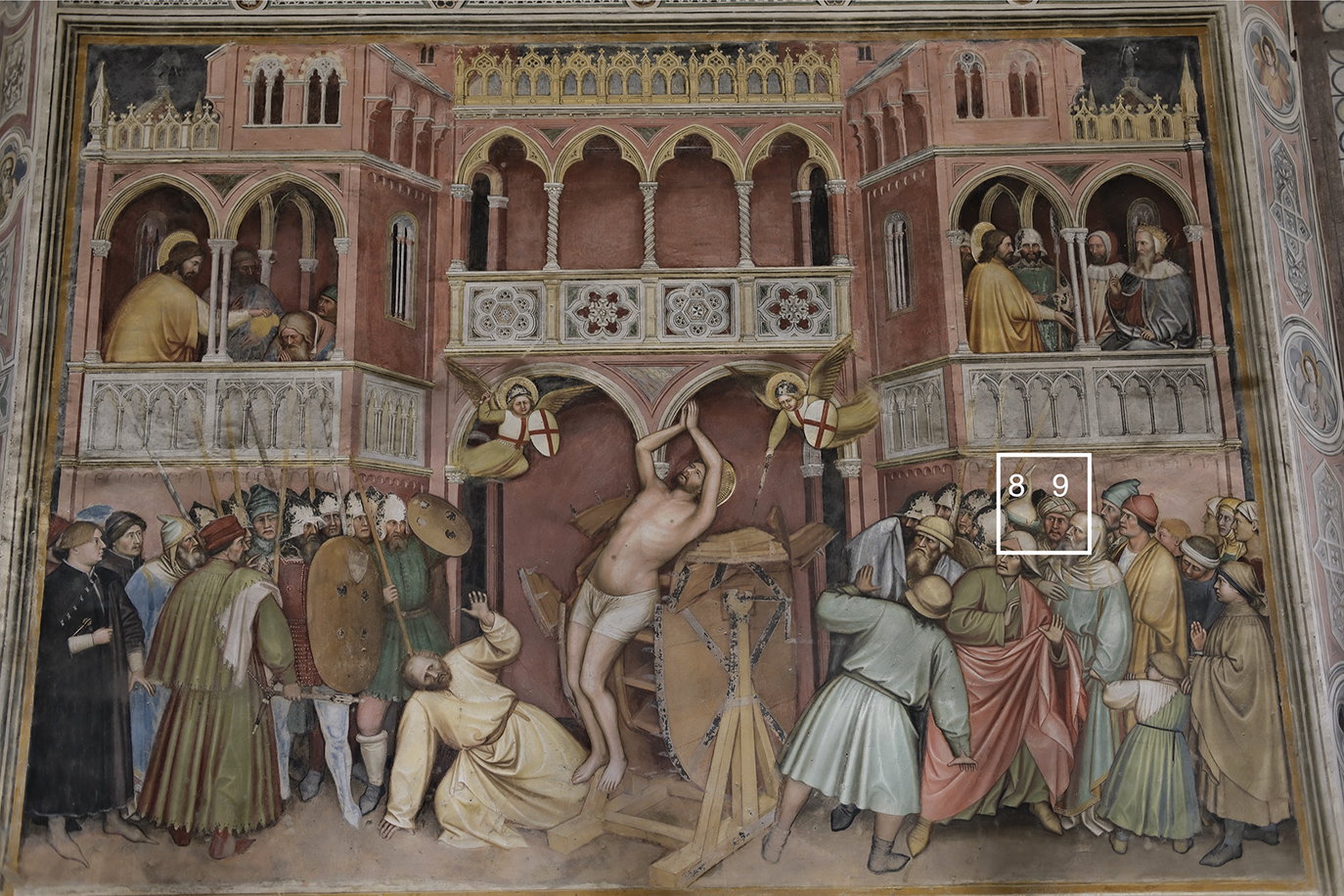Fresco showing Saint George bound to a wheel at the center, surrounded by soldiers, onlookers, and angels, with elaborate architecture and crowds on balconies. See long description.