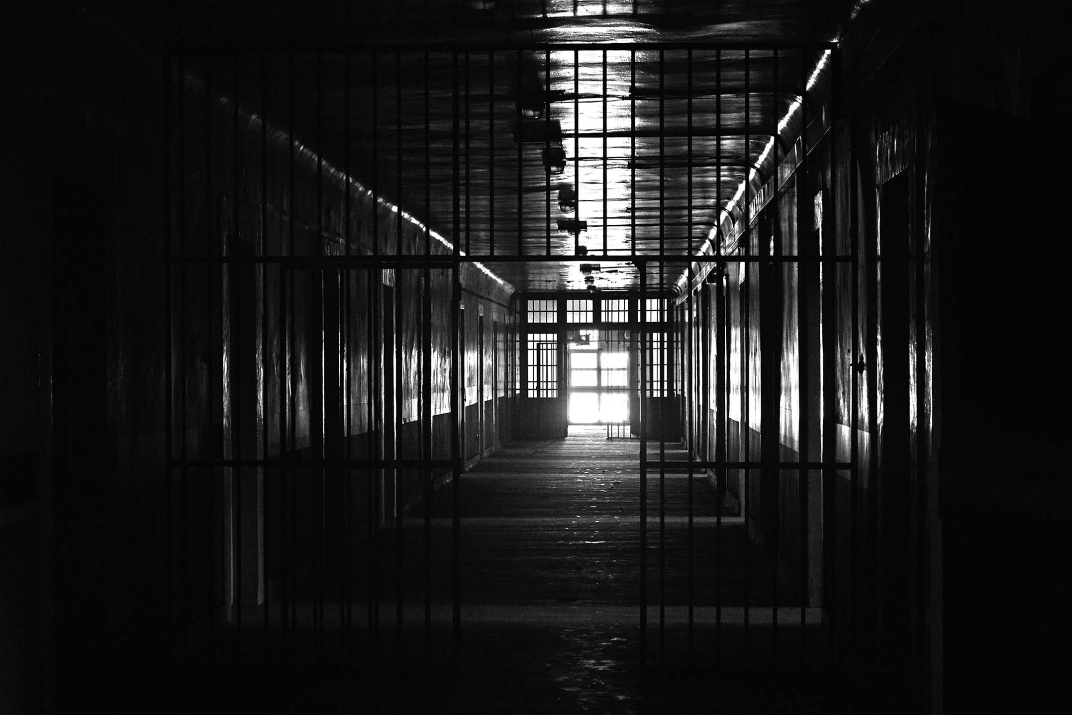 A black and white photo of a long corridor in a psychiatric hospital with bars separating the sections.
