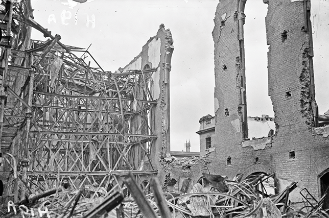 An interior view of a building that has suffered extensive fire damage. On the right, there are partial walls and windows are gone. To the left and in the foreground, we can see a mesh of warped metal.