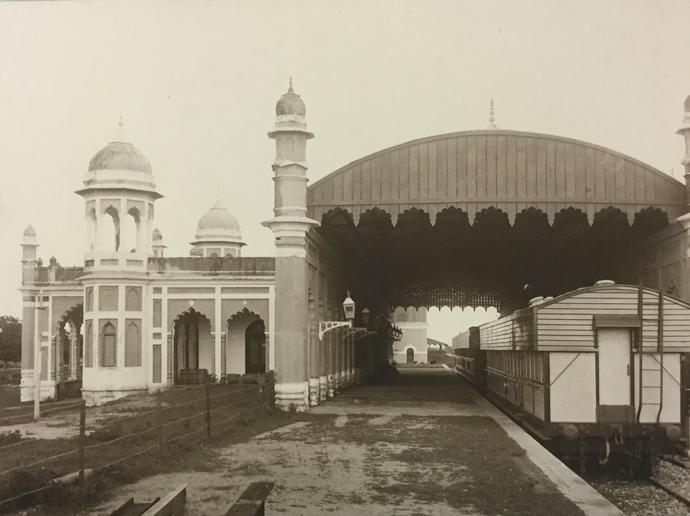 A railway station with an arched roof and adjacent building featuring domes and arches. See long description.