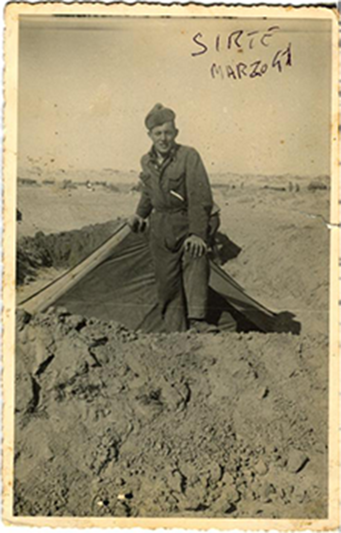 Raffaello standing beside a tent in a sandy area with 'Sirte Marzo 41' written above. See long description.