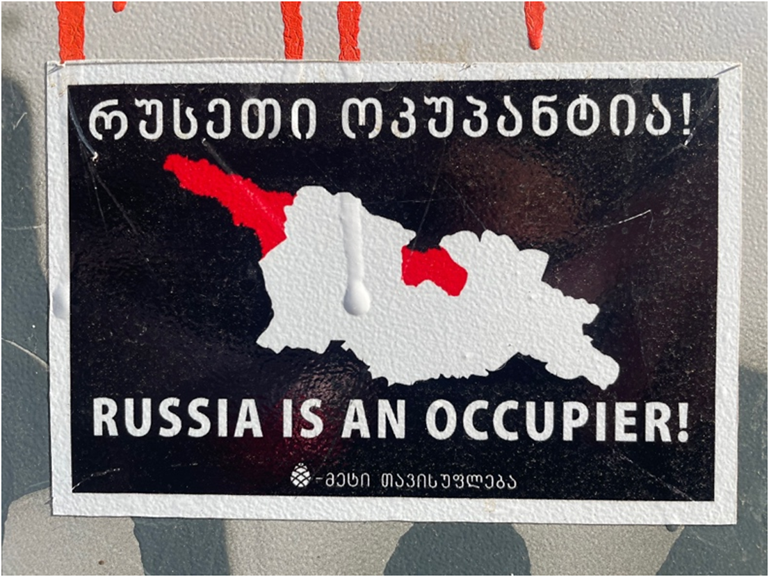 Photo of a black sticker with a white map of Georgia. Two regions are highlighted in red. Georgian text at the top and English text at the bottom reads RUSSIA IS AN OCCUPIER exclamation point.
