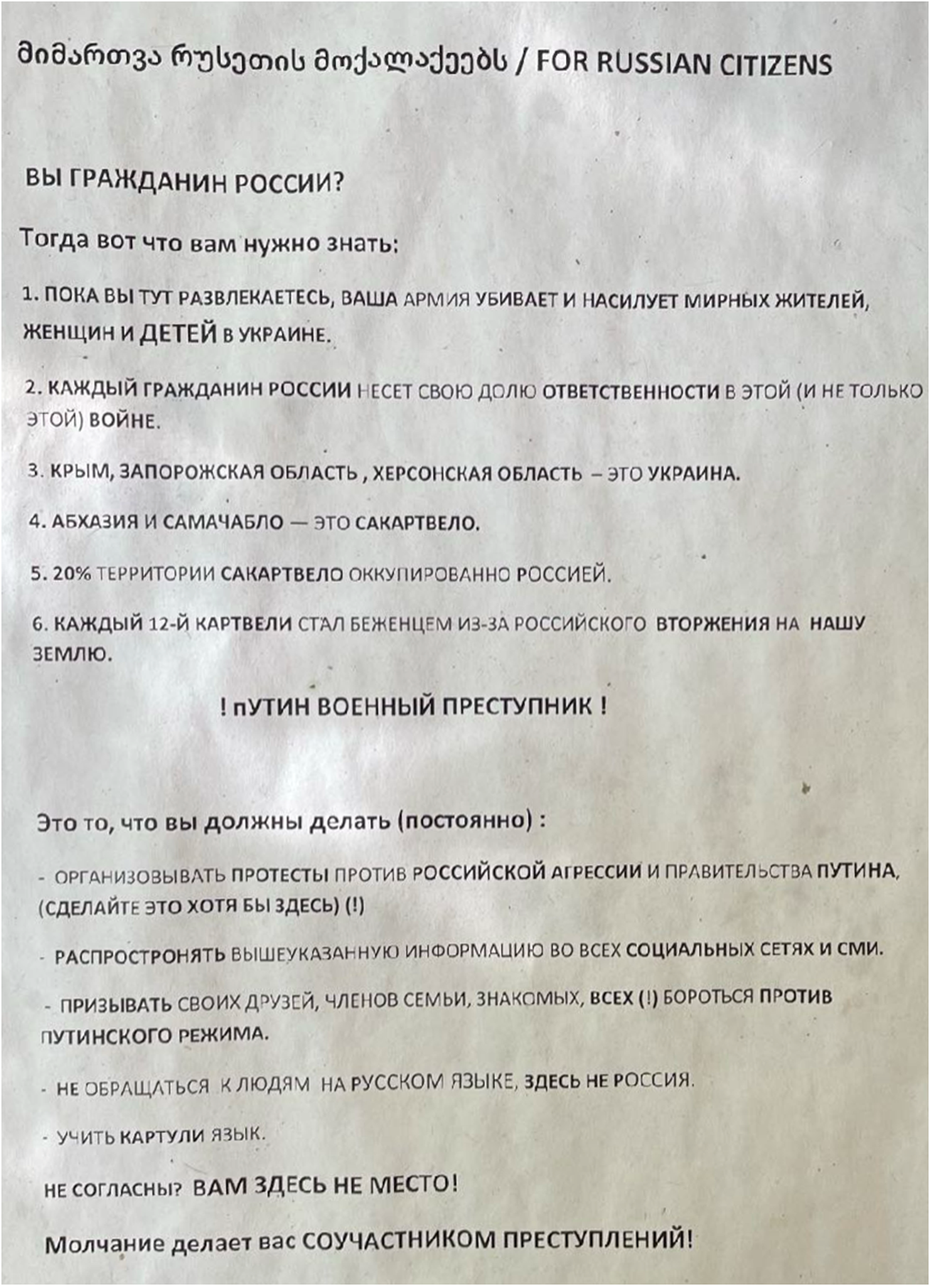 A photo of a printed notice in Russian and Georgian addressed to Russian citizens regarding the war in Ukraine and the occupation of Georgia. See long description.