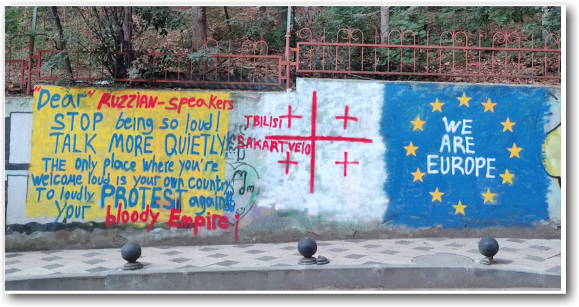 A photo of three graffiti panels. Left is a yellow block with a message to Russian speakers. Center is a white block with a red cross and Tbilisi Sakartvelo text. Right is a blue block with yellow stars and the text We Are Europe.