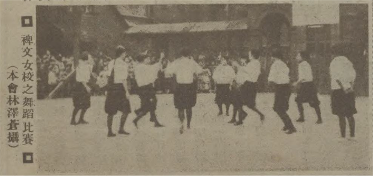 Photo of girls in uniform forming a circle while dancing outdoors with a crowd and buildings in the background.
