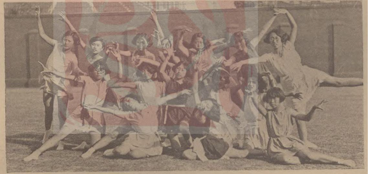 Photo of a group of women in mid-dance pose outdoors, arranged in layered rows with extended arms and legs, wearing light dresses.