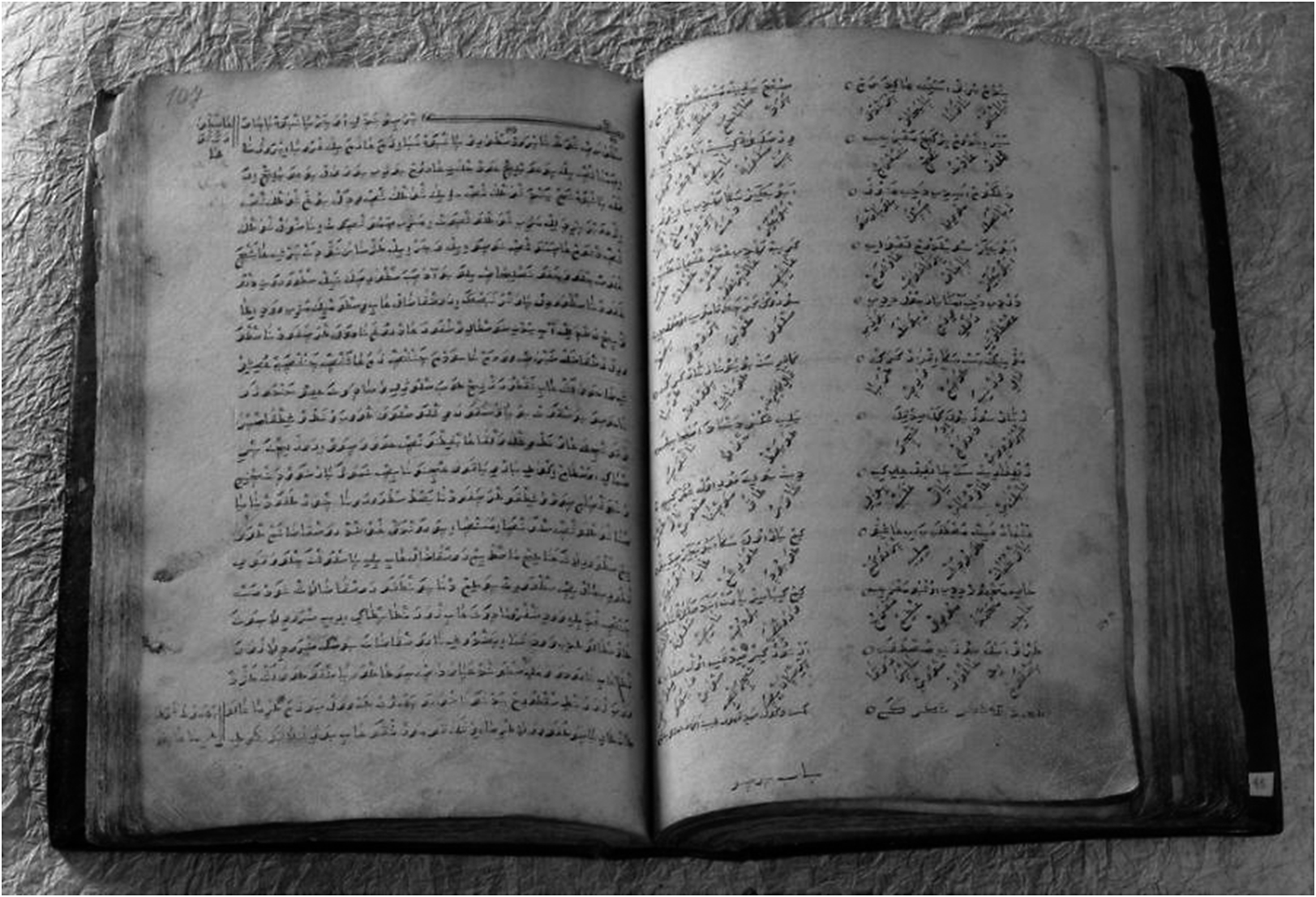 A black and white photo of an open manuscript featuring Arabic script on aged paper. See long description.