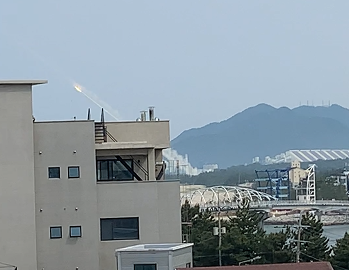 A missile launch seen from a building with mountains in the background. See long description.