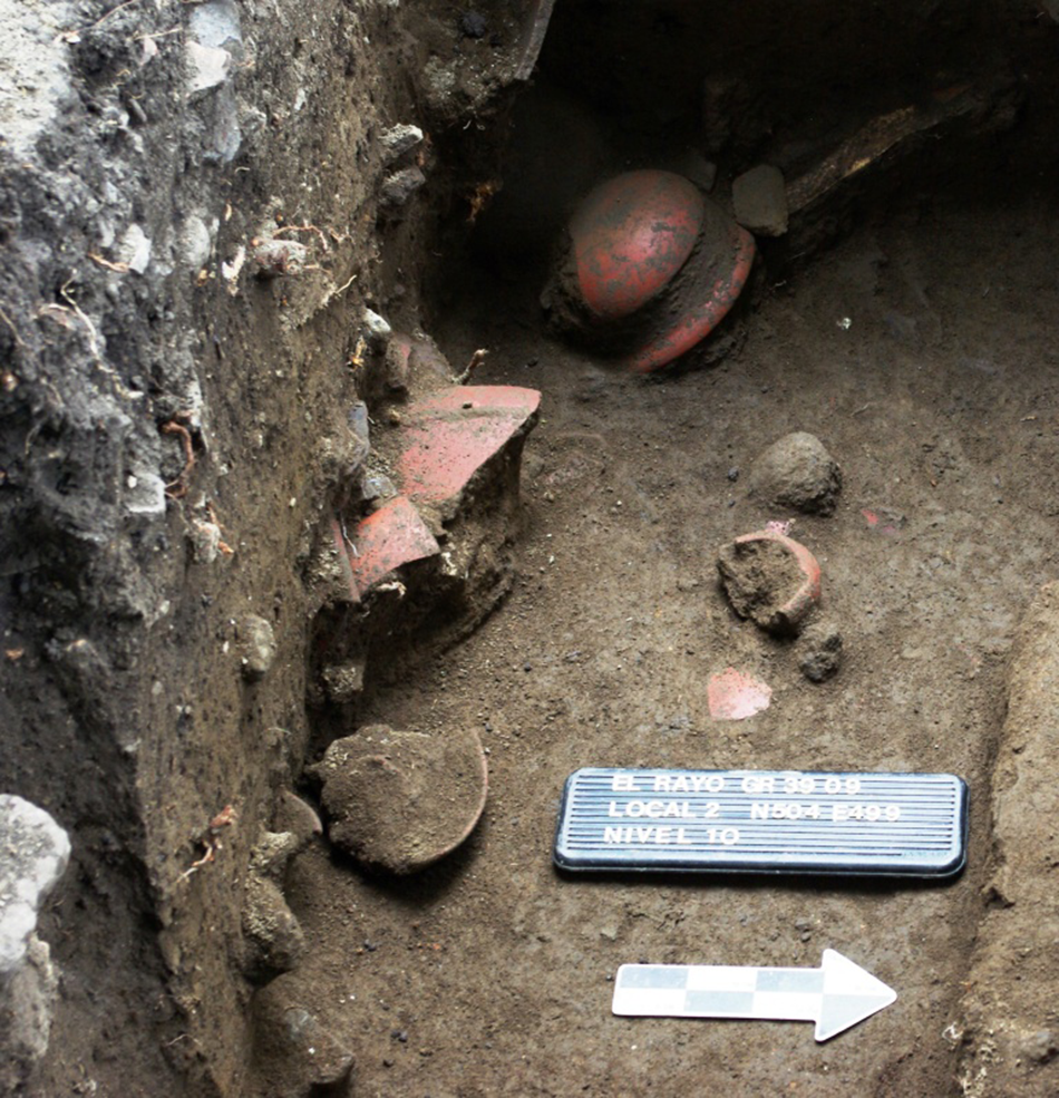 Archaeological excavation showing pottery fragments and a labeled marker. See long description.