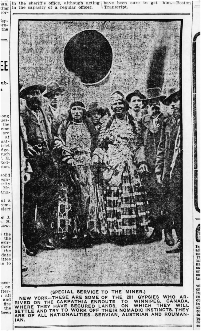 A photo of a group of Romani people, including several women in patterned dresses and men in hats, standing together next to a ventilation pipe on the deck of an ocean liner.