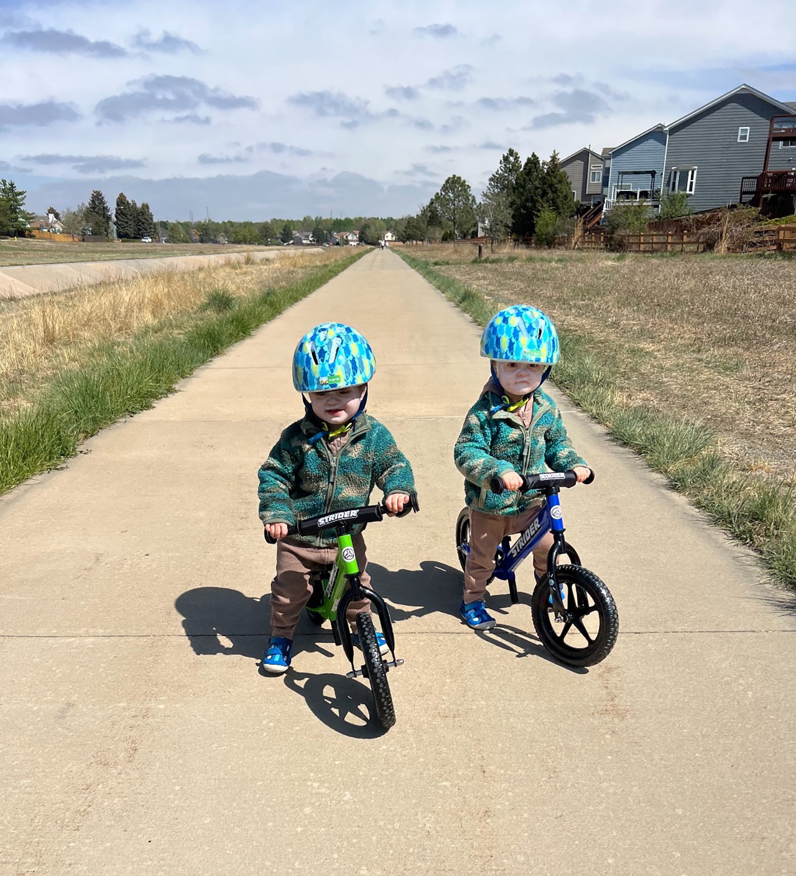 Two children wearing helmets riding bikes on a paved path.