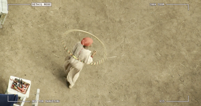 Aerial view of a young girl in a headwrap hula-hooping in a courtyard. A camera lens frames the shot. The girl has her back turned to the camera, but small details in the shot, such as tools in a toolbox next to her, are visible.