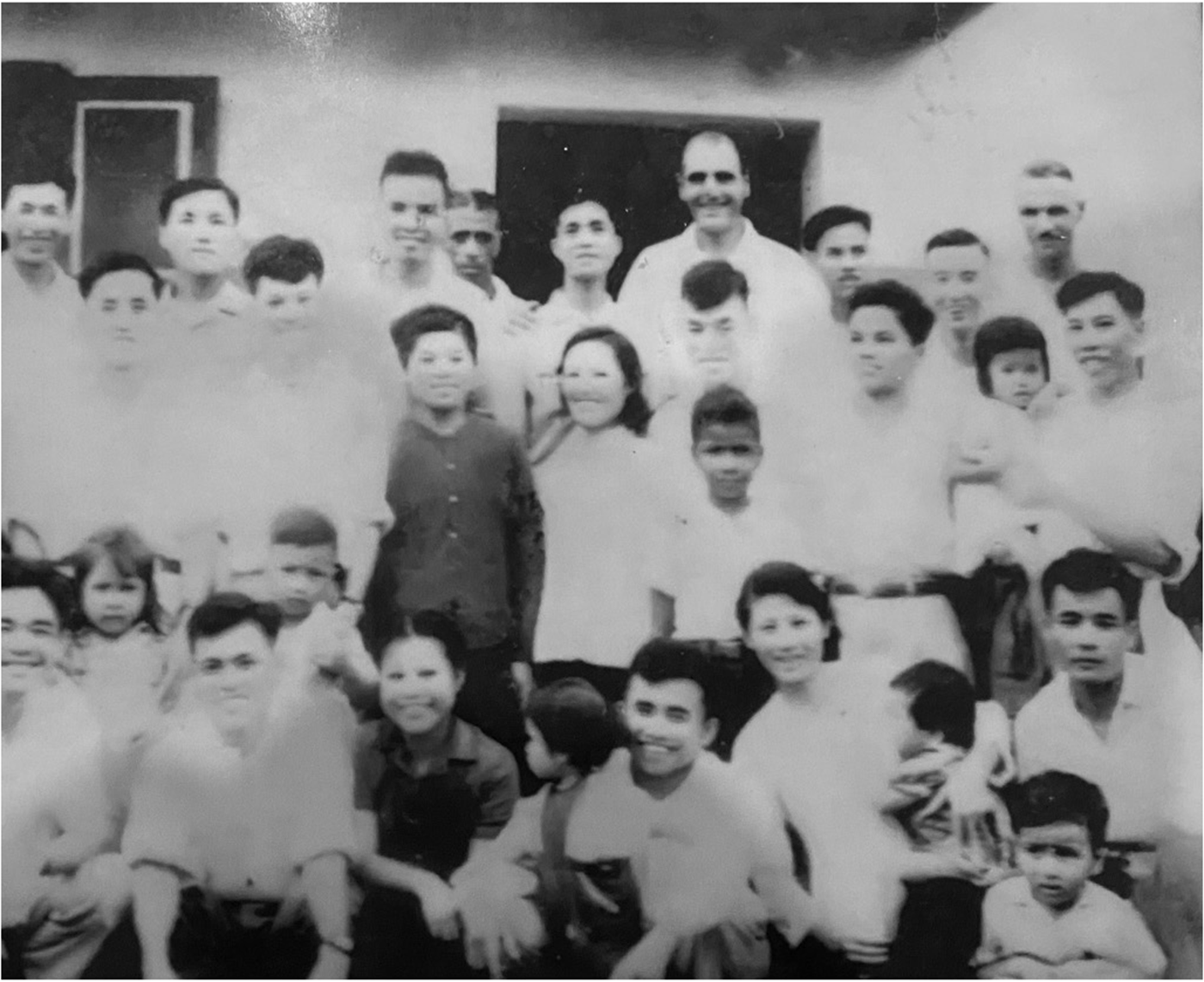 A group of people, including men, women and children, gathered in front of a building. See long description.