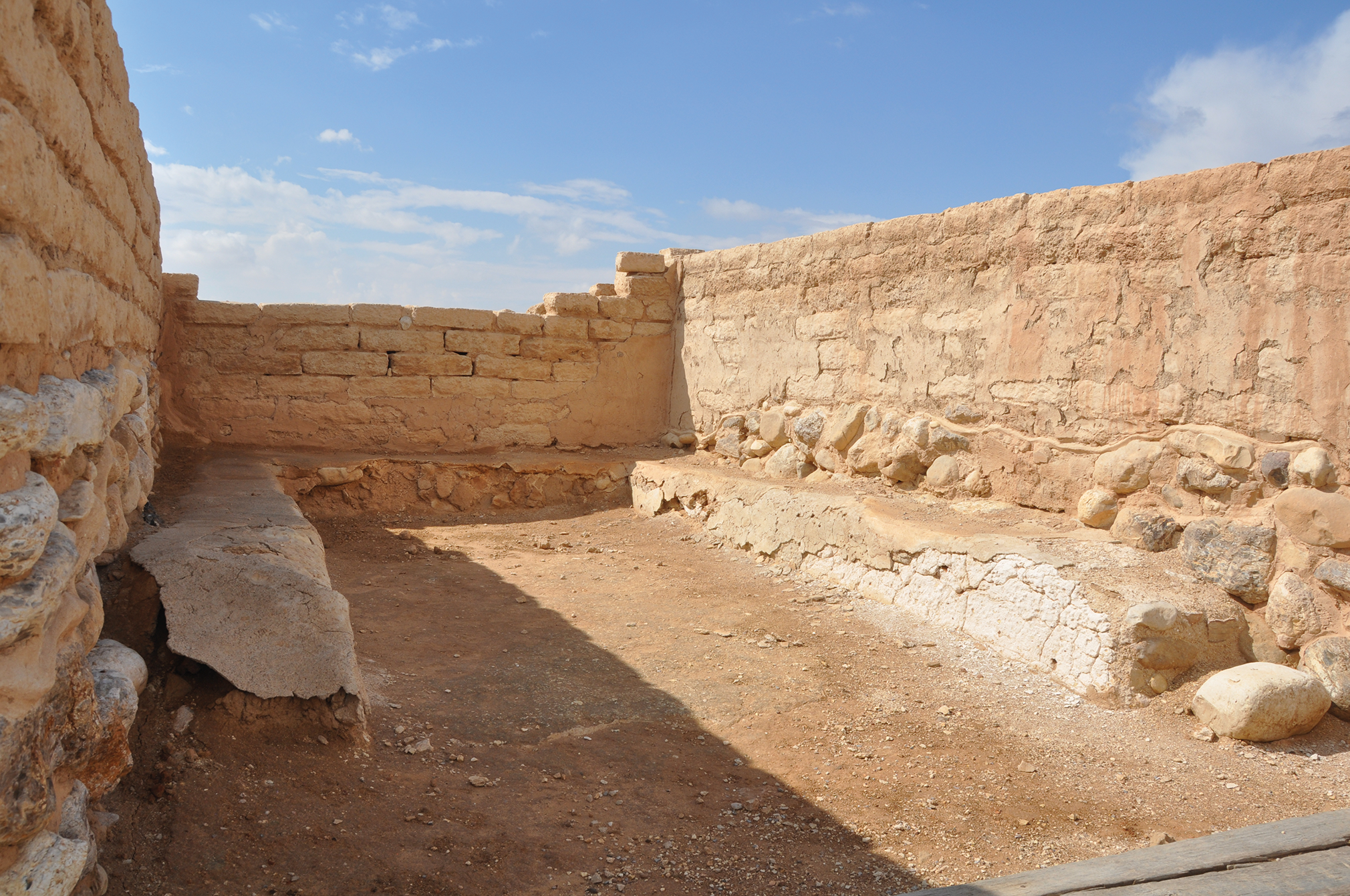 Ancient stone structure with walls and a dirt floor under a clear sky.
