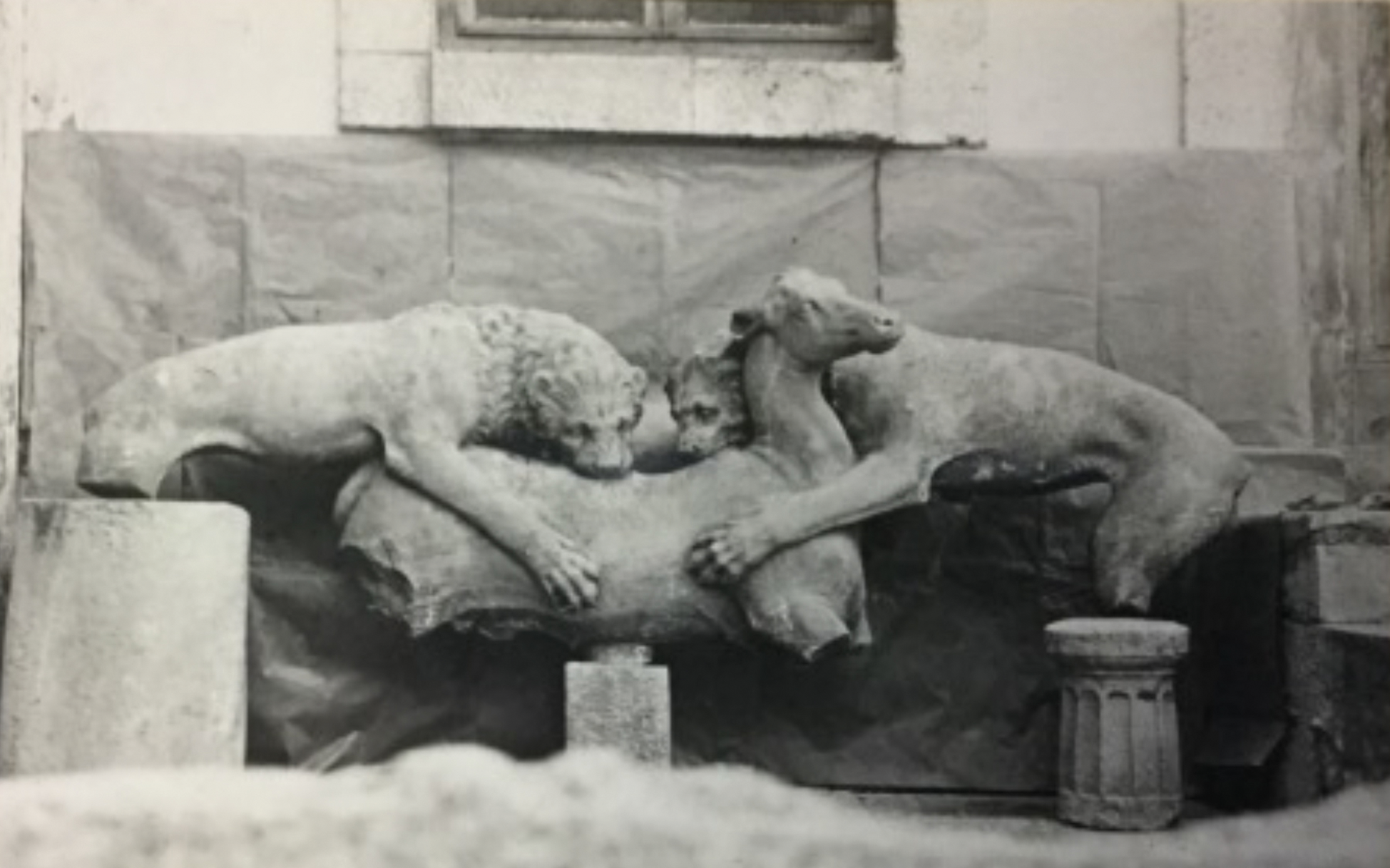 A black and white photograph of ancient ruins featuring a monumental base with sculptures of lions and a stag.