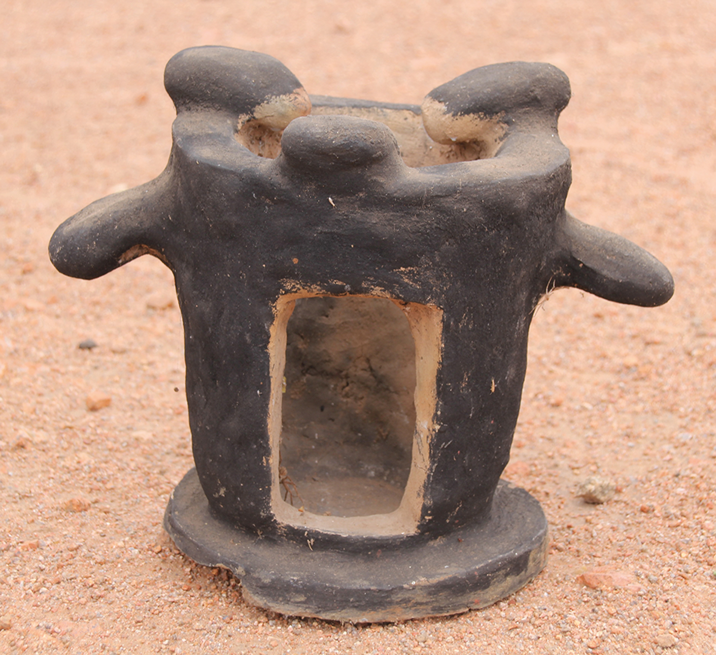 A black clay stove with a hollow center and four protruding handles.