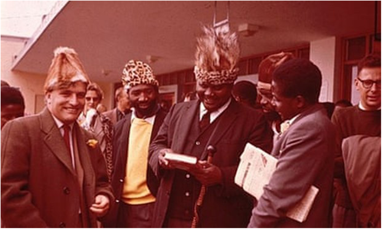 Five men standing together, some holding books and wearing traditional hats. See long description.