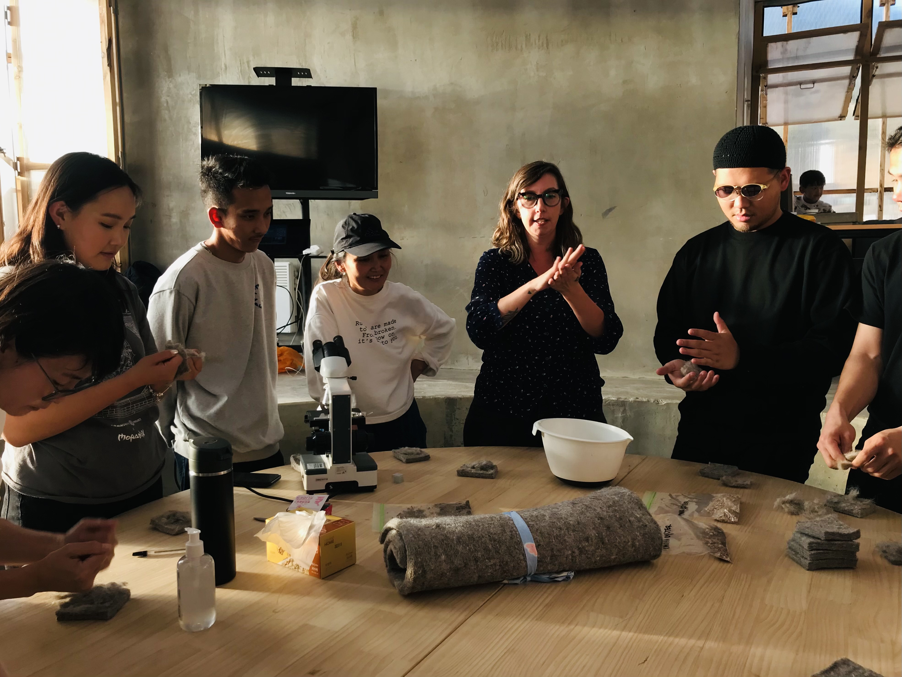Group of people working with materials on a table in a workshop setting.