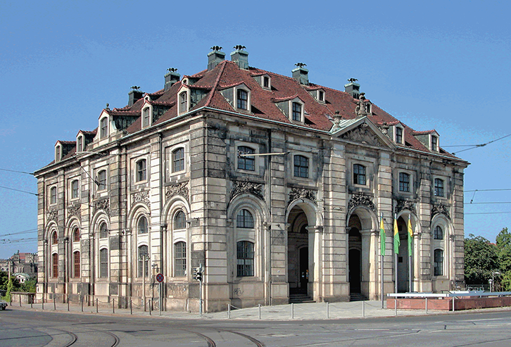 A building with a tall arched ground floor under an attic floor and a roof of red tile with dormer windows.