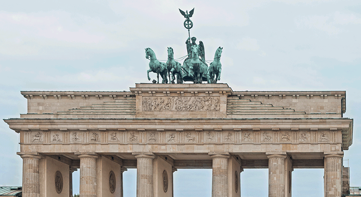 Photograph of the top of a monumental city gate with Doric columns supporting a quadriga on a plinth surrounded by a low stepped pyramid.