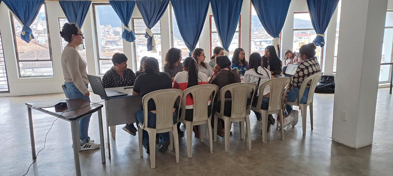 A group of women in a room with large windows, engaged in a discussion around a table.